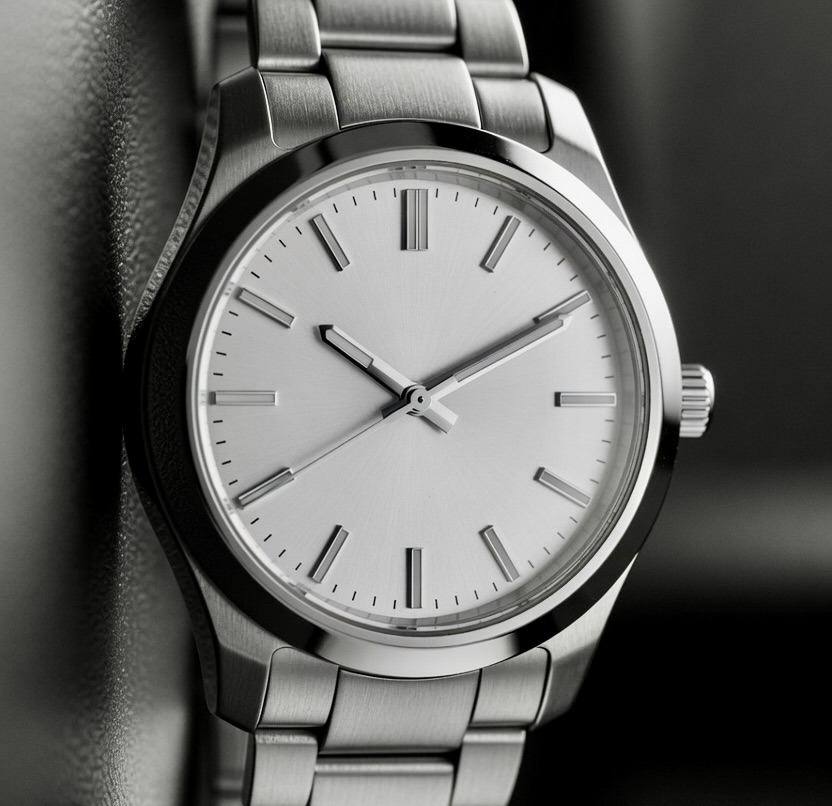 A close-up of a steel wristwatch with a plain silver dial — the quiet instrument of a window that opens and closes without announcement.